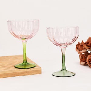 Puede incluir: Dos copas con tallo de color rosa y verde con un dise&ntilde;o acanalado. Las copas est&aacute;n sobre una superficie de madera.
