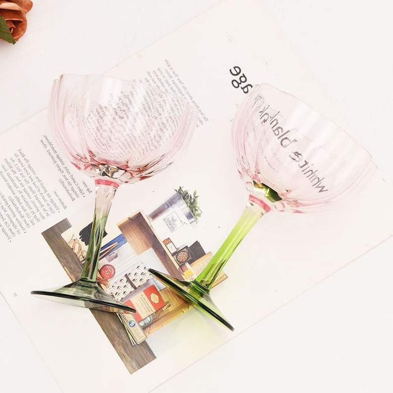 Puede incluir: Dos copas de vidrio rosa con tallos verdes. Las copas tienen un dise&ntilde;o texturizado y ondulado y el texto "White & Pink" est&aacute; impreso en una de las copas.