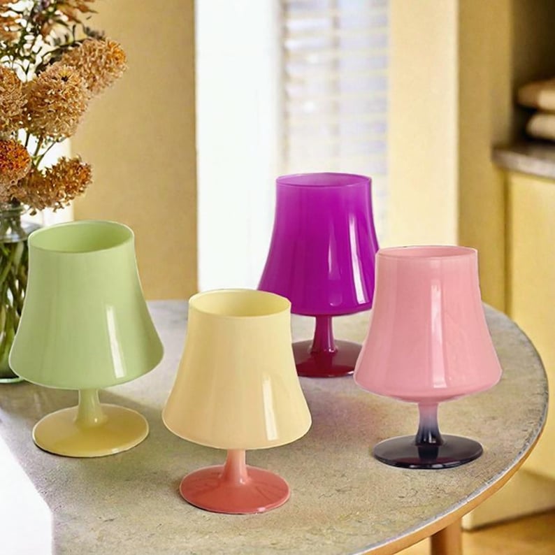 May include: Four stemmed glasses with a lampshade design. The glasses are in different colors: yellow, pink, light green, and purple.