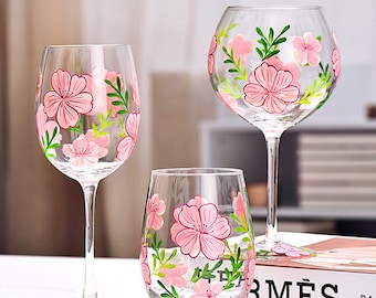May include: Set of three hand-painted wine glasses with pink floral designs. The glasses are clear and have a delicate stem. The flowers are pink and green and have a whimsical feel.