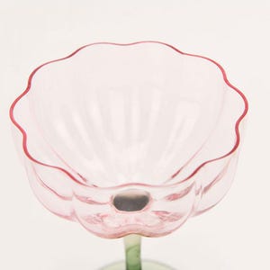 Puede incluir: Una copa de vidrio rosa con un borde festoneado y un tallo transparente. La copa est&aacute; dise&ntilde;ada para parecerse a una flor.