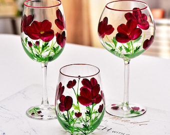 May include: Three glass wine glasses with red floral designs. The glasses are clear and have a red rim. The flowers are painted on the glass and are red with green leaves.