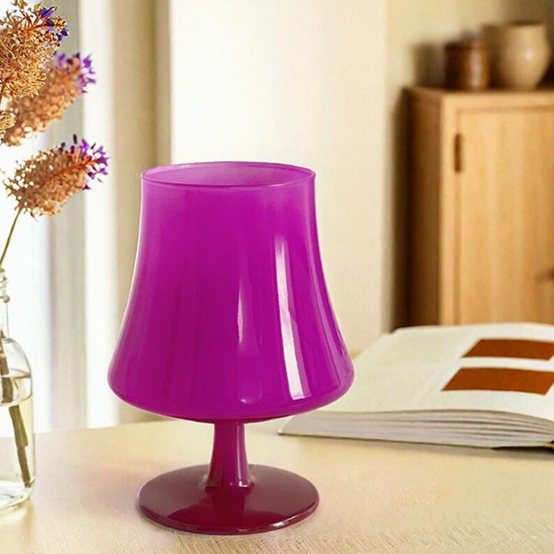 May include: A purple glass goblet with a wide bowl and a short stem. The goblet has a shiny, glossy finish.