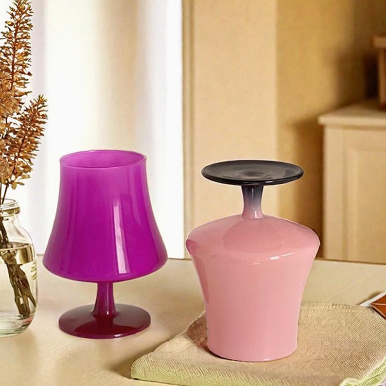 May include: Two glass cups, one is pink and the other is purple. The pink cup has a black rim and a black stem. The purple cup has a wide base.