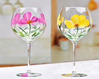 May include: Two hand-painted wine glasses with floral designs. One glass features pink flowers and the other features yellow flowers.