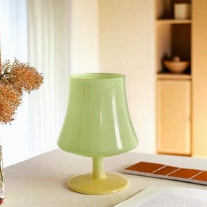 May include: A pale green glass vase with a wide, flared base and a rounded, bell-shaped top. The vase has a yellow-toned base.