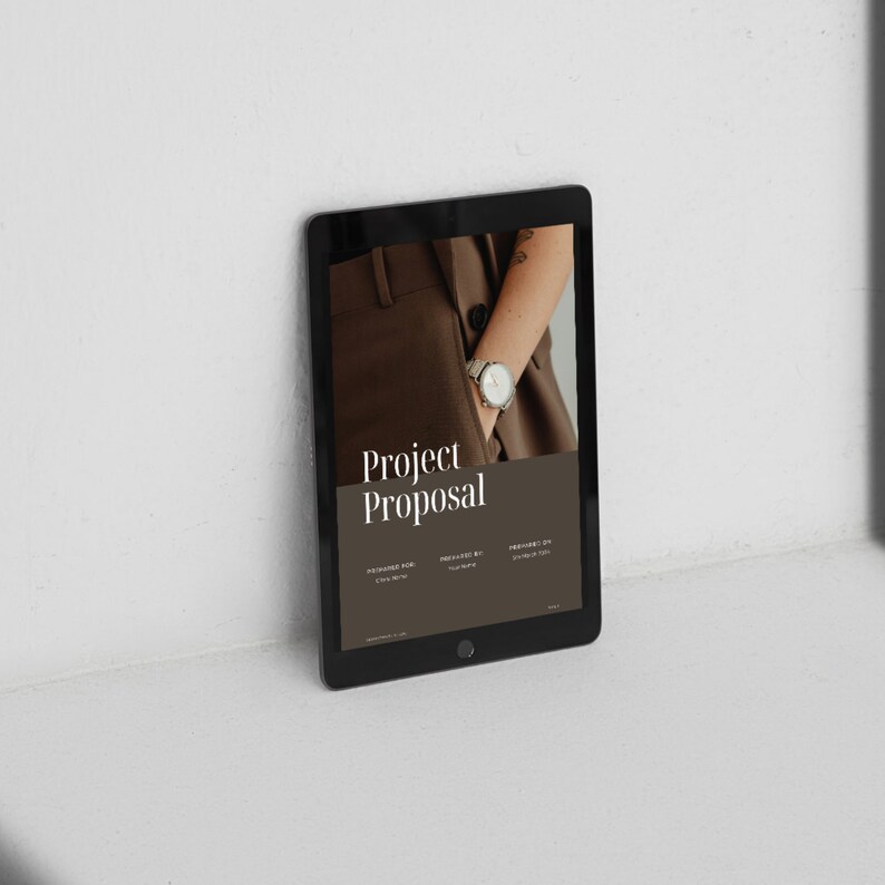 K&ouml;nnte beinhalten: Ein schwarzes Tablet-Computer, auf dem ein Projekt-Vorschlagsdokument mit dem Titel "Project Proposal" angezeigt wird. Das Dokument hat einen braunen Hintergrund mit einem Foto eines Arms, der eine Uhr tr&auml;gt.