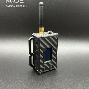 Puede incluir: Un dispositivo rectangular negro con una pequeña pantalla y una antena negra. El dispositivo está hecho de PLA de fibra de carbono y tiene una superficie texturizada. El texto "NANO NODE CARBON FIBER PLA" está impreso en el dispositivo.