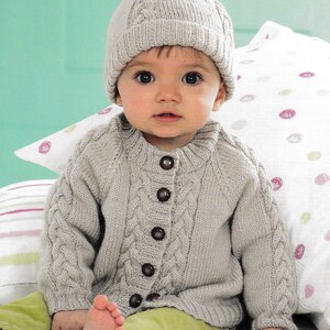 Può includere: Un cardigan e un cappello coordinato per neonati, lavorati a maglia grigio chiaro, con un pompon. Il cardigan presenta un motivo a trecce sul davanti e sulle maniche, con bottoni marrone scuro. Il bambino indossa pantaloni verde chiaro.