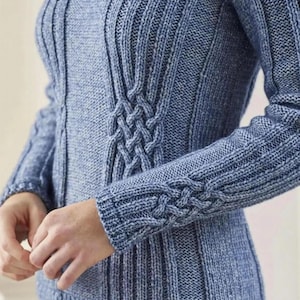 May include: A light blue knitted sweater with a textured design. The sweater features vertical ribbing and a cable knit detail on the sleeves and bodice. The sleeves are long, and the sweater has a fitted silhouette.
