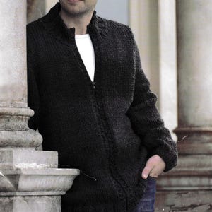 Puede incluir: Un suéter con cremallera de punto gris oscuro con cuello alto. El suéter se usa sobre una camiseta blanca. La persona lleva vaqueros azules. El suéter tiene un aspecto texturizado y una cremallera de largo completo.