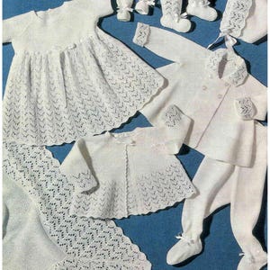 May include: A set of white knitted baby clothes, including a dress, a cardigan, a hat, booties, and trousers. The clothes are made with a delicate lace pattern.