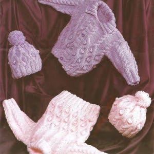 May include: A light purple knitted baby sweater and matching hat with a pom-pom. The sweater has a cable knit design with decorative bobbles. A second set of baby clothes in pink includes a hat with a pom-pom and a pair of booties.