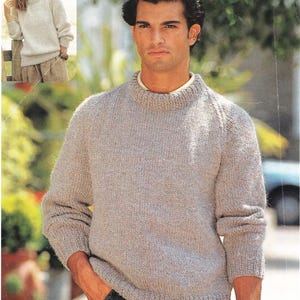 Può includere: Un maglione di maglia grigio chiaro con girocollo e maniche lunghe. Il maglione ha orlo e polsini a coste. Una donna indossa un maglione simile in un'immagine più piccola. L'uomo indossa un orologio.