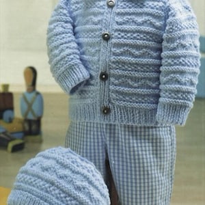 May include: A baby's light blue knitted outfit, comprising a collared cardigan with three buttons, a matching hat, and checkered trousers. The cardigan and hat feature a textured pattern. The outfit is designed for a baby or toddler.