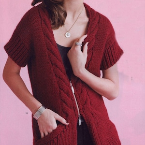 May include: A burgundy knitted vest with short sleeves, a full-length zip, and two front pockets. The vest features a cable knit design along the front and hood. The model is wearing a silver bracelet and a necklace with a pendant.