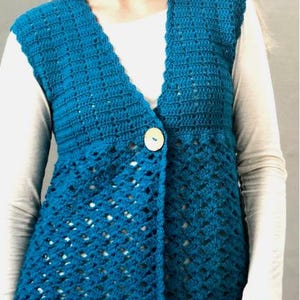 Puede incluir: Un chaleco de ganchillo azul turquesa con cierre de botón. El chaleco presenta un patrón de puntada texturizada en la parte superior y un diseño calado en la mitad inferior. Un botón grande, redondo y blanquecino asegura el frente. El chaleco se usa sobre una camisa blanca de manga larga.