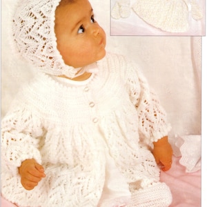 Könnte beinhalten: Ein Baby in einem weißen Strick-Outfit, bestehend aus einer Haube, einer Strickjacke und Babyschuhen. Das Outfit hat ein zartes Lochmuster. Das Bild zeigt auch ein passendes Set Babykleidung mit Haube, Fäustlingen und einem Kleid.