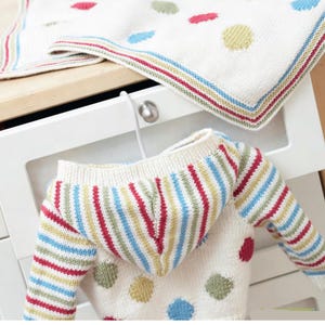 May include: A cream-colored knitted baby blanket and hooded sweater set. The blanket has colorful polka dots and a striped border. The sweater features striped sleeves and hood, with polka dots on the body. The set is made of soft, knitted material.