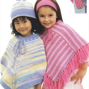 May include: Two young girls wearing knitted ponchos and hats. One girl wears a blue and pastel striped poncho and hat. The other girl wears a pink and white striped poncho and a pink headband. The ponchos have fringe.
