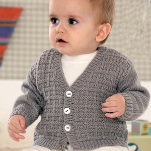 Könnte beinhalten: Graue, gestrickte Baby-Strickjacke mit strukturiertem Webmuster und V-Ausschnitt. Die Strickjacke hat drei weiße Knöpfe vorne und lange Ärmel. Das Baby trägt ein weißes Shirt darunter.