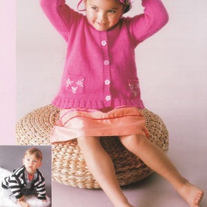 May include: A girl in a pink knitted cardigan with floral details and a matching headband. She is seated on a woven ottoman, wearing a peach skirt. An inset shows a baby in a black and white striped cardigan. The cardigan has white buttons.