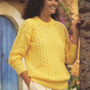 Könnte beinhalten: Ein gelber Strickpullover mit einem zarten Lochmuster. Der Pullover hat einen runden Ausschnitt und lange Ärmel.