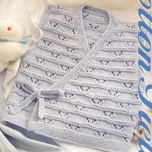 May include: A light blue knitted baby wrap with a wrap-around design and a bow closure. The wrap features a textured pattern with small openings, and is made of soft yarn. The baby wrap is designed to keep the baby warm and comfortable.