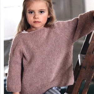 May include: A young child wearing a mauve-colored knitted sweater with three-quarter sleeves and striped pants. The sweater has a ribbed hem and cuffs. The child is leaning against a wooden ladder.
