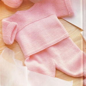May include: A light pink knitted baby outfit, including a sweater and pants, is displayed. The sweater has long sleeves and a ribbed collar and cuffs. The pants are also knitted in the same light pink yarn. A ball of pink yarn is in the background.