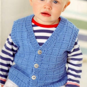 May include: A baby in a light blue knitted waistcoat with a V-neck and button fastening. The waistcoat features a textured design and is worn over a striped top with a red collar. The buttons are light brown.