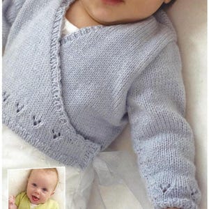 May include: A pale blue knitted baby cardigan with a wrap-style design. The cardigan has decorative cut-out details on the edges and cuffs. The baby is wearing a white undershirt. A smaller image shows a baby wearing a similar green cardigan.