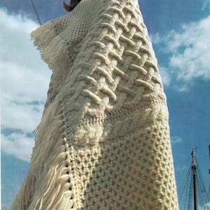 May include: A white knitted throw blanket with a cable knit pattern and fringe. The blanket is draped over a person's shoulders.