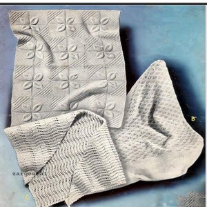 May include: Three white crocheted baby blankets with different patterns. The blanket on the left has a simple wave pattern, the blanket in the center has a flower pattern, and the blanket on the right has a diamond pattern.