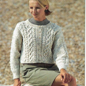 May include: A white cable knit cardigan with a button closure. The cardigan has a textured pattern and is worn by a person with blonde hair.
