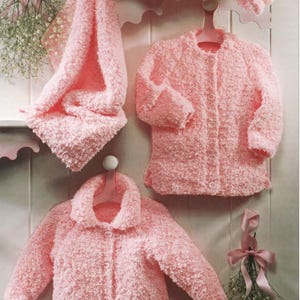 May include: A set of soft, pink, fuzzy children's clothing, including a jacket, a hat, and a blanket. The jacket has buttons and a collar. The items are hanging on a wall with decorative accents, suggesting a nursery or children's room theme.