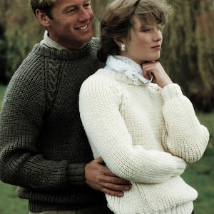 Puede incluir: Una pareja lleva suéteres de punto. El hombre lleva un suéter gris oscuro con un patrón de punto de cable. La mujer lleva un suéter blanco con un patrón de punto fino. El texto "Diploma high performance Aran" está en la parte inferior de la imagen.