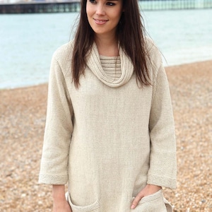 May include: A cream-colored knitted sweater with a cowl neck and two patch pockets. The sweater is made of a soft, textured yarn.