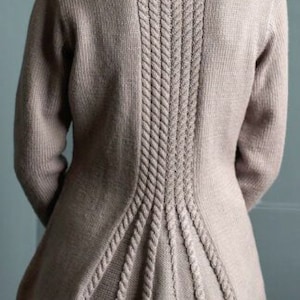 Puede incluir: Un suéter de punto marrón claro con un diseño de punto de cable en la espalda. El suéter tiene un cuerpo ajustado y un dobladillo acampanado.