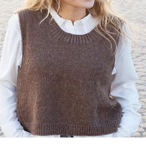 Può includere: Un gilet marrone lavorato a maglia con scollatura e orlo a coste. Il gilet è indossato sopra una camicia bianca con colletto. Il gilet è di colore pieno e sembra essere realizzato in un materiale morbido e caldo. Stile casual.