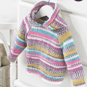 Könnte beinhalten: Ein mehrfarbiger Baby-Hoodie mit Kapuze und langen Ärmeln, präsentiert auf einem weißen Kleiderbügel. Der Pullover hat horizontale Streifen in Rosa, Blau, Gelb und Lila. Das Design beinhaltet horizontale Streifen und strukturierte Strickmuster.