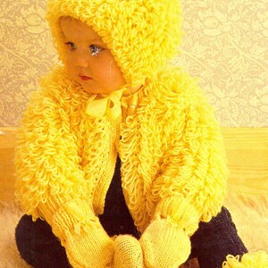May include: A baby wearing a bright yellow knitted outfit, including a hooded jacket, mittens, and booties. The outfit has a textured, looped design and a small bow at the neck. The baby is wearing black pants.