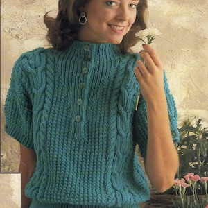 Puede incluir: Un suéter de punto azul turquesa con un patrón de trenza y cuello alto. El suéter tiene una abertura de botones y mangas cortas.