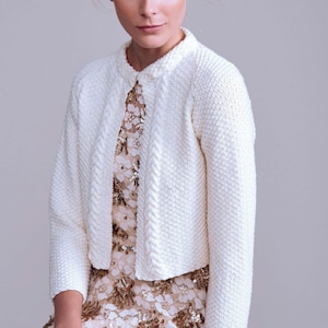 Könnte beinhalten: Ein weißer Strickcardigan mit einem Zopfmuster auf der Vorderseite. Der Cardigan hat eine verkürzte Länge und lange Ärmel.