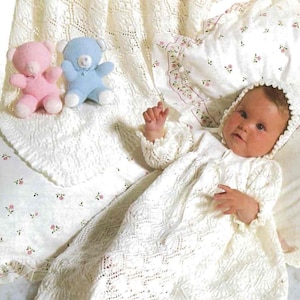 Peut inclure: Un bébé vêtu d'une robe et d'un bonnet en tricot blanc et dentelle est allongé sur une couverture blanche avec un motif assorti. Deux petits ours en peluche, un rose et un bleu, sont à proximité. La couverture et l'oreiller ont des motifs floraux.