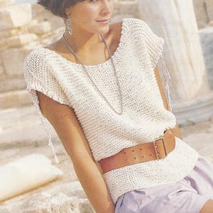 May include: A white crocheted top with a scoop neck and short sleeves. The top has a loose fit and is cinched at the waist with a brown leather belt.