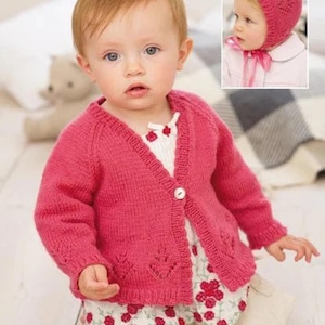 以下が含まれることがあります： 明るいピンク色のニットカーディガンを着た赤ちゃん。白いボタンが1つ付いており、葉の形をした切り抜きがあります。赤ちゃんはまた、赤い花のディテールとマッチするショートパンツが付いた白いトップスを着ています。小さなインセット画像には、ニットのピンク色のボンネットが表示されています。