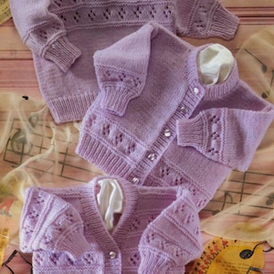 May include: Three lavender-colored knitted sweaters. One is a crew neck with decorative stitching, and the other two are cardigans with button closures. The sweaters have long sleeves and are displayed on a light brown surface.