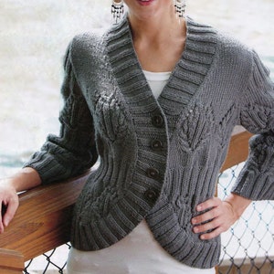 Puede incluir: Un cárdigan de punto gris con un patrón de trenza y cuello en V. El cárdigan tiene botones en la parte delantera y una longitud ligeramente recortada.