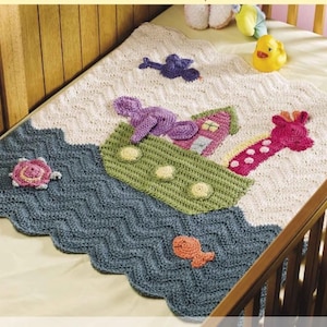 May include: A crocheted baby blanket with a blue and white chevron pattern. The blanket features a green, pink, and yellow crocheted ark with a purple elephant, a pink giraffe, and a yellow bird. The ark is on a blue and white wave pattern.